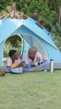 Vertical video: Youth offering cup sparking dad and son high-fiving, laughing, sipping mugs at tent