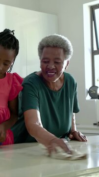 Vertical video: Spraying grandchild in pink dress, gran wiping island, cleaning with sprays and rag