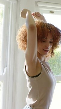 Vertical video: Stretching curly woman lifting arms, sun at window, friend copying, linking hands
