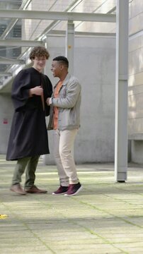 Vertical video: Walking grad in gown holding cap sparking friend cheering hugging leaving on campus