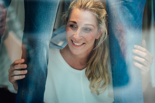 Modern portrait of a blonde woman looking through a fashion store window surrounded by reflections and stylish city architecture.