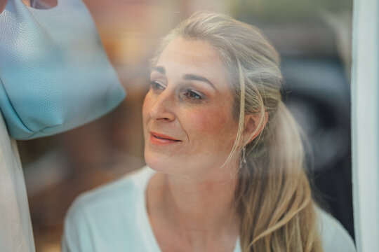 Attractive blonde woman looking into a fashion store window with elegant reflections and contemporary urban shopping lifestyle.