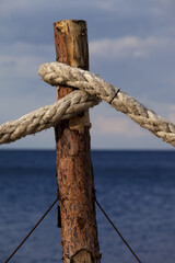 Fototapeta premium Old rope knotted on pine post and sea with sky