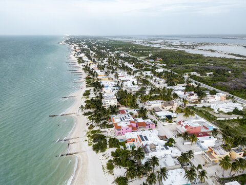 Aerial view of the coastal town of Chuburna featuring colorful houses, sandy beaches, palm trees, and wooden groynes extending into the turquoise sea in Chuburna, Yucatan, Mexico.