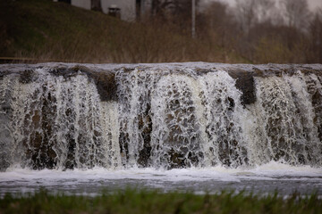 Waterfall cascading over rocks at Venta River in Kuldiga, Latvia, surrounded by grass and trees, showcasing natural beauty of the landscape © Riga Frames
