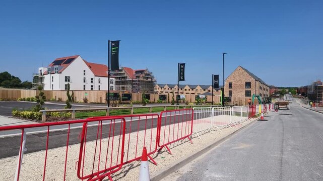Winchester Hampshire England UK. 14.06.2026. Video. Construction of modern residential buildings progresses with heavy machinery and safety barriers on a sunny day