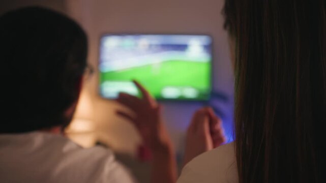 People at home watching a football match, reacting emotionally and celebrating, raising their hands in excitement. Friends celebrating a football goal at home, cheering and clinking beer glasses