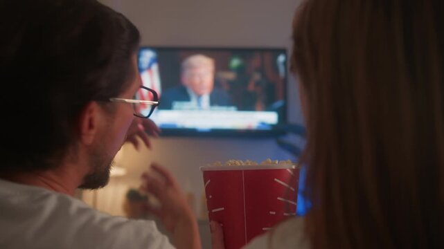 Couple sitting on a sofa in the living room watching TV with popcorn. Man throws popcorn toward the screen, expressing annoyance and frustration while watching news, movies or TV series. Home