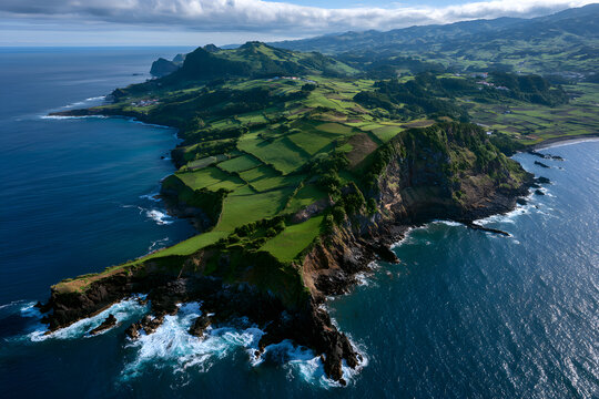 Aerial view of the rocky coastline of the Azores with green agricultural fields on the cliff, and ocean waves
