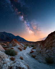 Obraz premium Starfield arches over arid canyon floor. Mountains frame twilight's soft orange glow. Dust-laden rocks line a quiet, winding path. Hue city, Vietnam - 02 June 2026