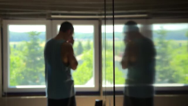 Depressed teenager in a dark bedroom staring at his reflection. Hiding face in hands and despairing