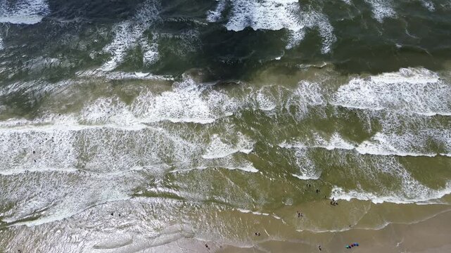 Gentle breakers roll across shallow coastal waters, washing over fine sand where visitors swim. Rhythmic white foam lines contrast with murky dark depths moving toward open horizon, Freeport, TX