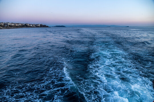 Foam wake trace on blue sea water behind a ferry boat boat in Istanbul. Ship track wave pattern in sunset twilight, maritime transport, evening travel background, April, Turkey.