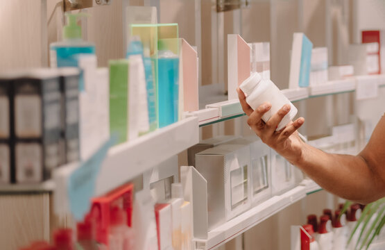 Close up of hand holding medicine bottle choosing product from pharmacy shelf