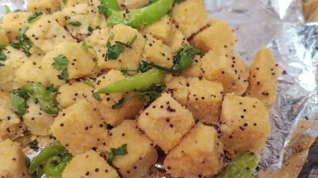 Close-up of Fresh Yellow Khaman Dhokla with Green Chili and Mustard Seeds
