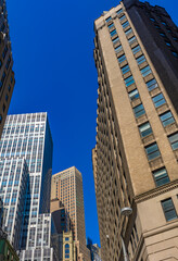 Fototapeta premium Modern and historic skyscrapers rising above downtown street under a clear blue sky