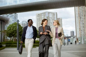 Fototapeten Musik Group of three people walk together in a city area during the afternoon  © BGStock72