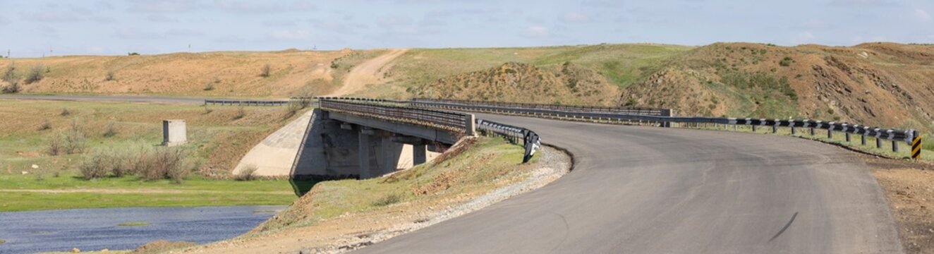paved road and a bridge with a bend crossing the river
