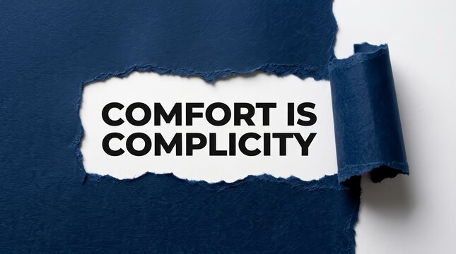 Text reading Comfort Is Complicity displayed through a hole in textured blue paper.