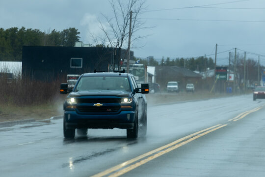 La Tuque, Canada, 07 May 2026 : A blue Chevrolet Silverado pickup truck drives on a wet road during a rainy day.