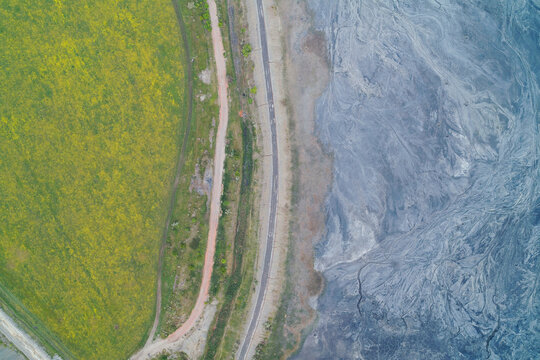 Industrial slag heap slope with toxic waste erosion runoff next to green agricultural field drone shot