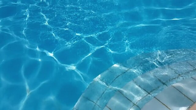 Refreshing blue water in a swimming pool with bright sunlight caustics and underwater tiled stairs