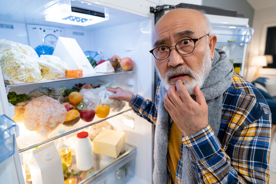 Concerned senior man discovering moldy food inside refrigerator highlighting food spoilage, refrigerator maintenance and household hygiene