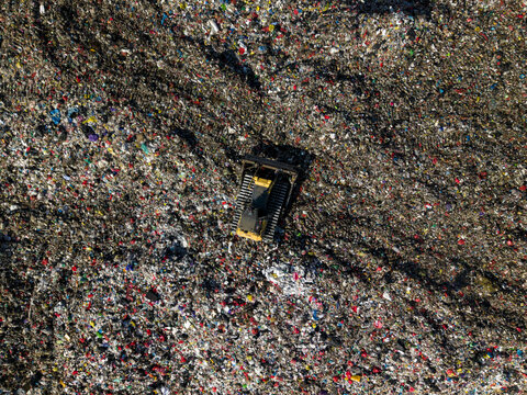 Aerial view of TPA Suwung landfill with a bulldozer working among piles of waste in Kecamatan Denpasar Selatan, Bali, Indonesia.