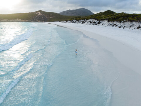 Aerial view of Hellfire Bay with a person standing in turquoise water along the white sand beach, surrounded by dunes in Cape Le Grand National Park, Western Australia, Australia.