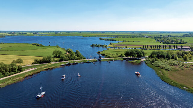 Aerial view of the Sneekermeer lake and canal system near Terherne, featuring sailboats on the water, green meadows, and a small bridge in Terherne, Friesland, Netherlands.