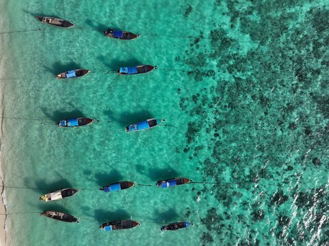 Aerial view of Koh Lipe Pier with traditional long-tail boats moored in clear turquoise water over coral reefs in Tambon Ko Tarutao, Chang Wat Satun, Thailand.