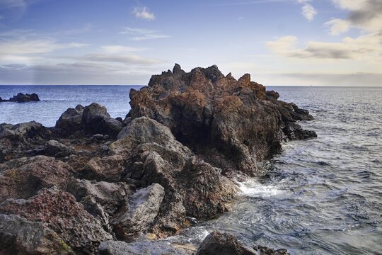 Rough rock formation jutting into the sea surrounded by waves under a slightly cloudy sky, Puerto del Carmen Lanzarote