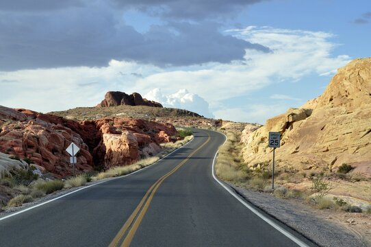 Narrow road with road sign snakes through red rocks under dramatic clouds in the sky, Valley of Fire State Park, Nevada, USA