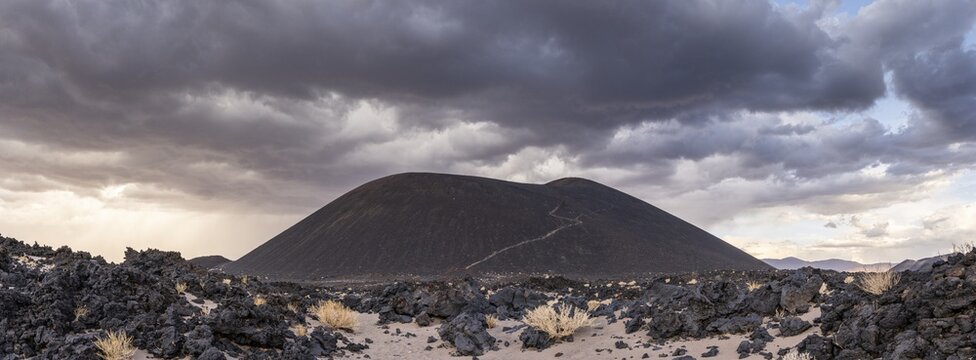 A volcanic hill rises under dramatic clouds in the middle of a rocky desert, Argentina, volcanoes, lava field, Antofagasta