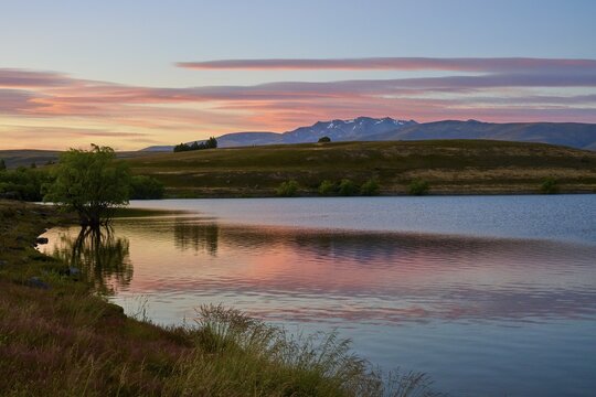 Reflecting lake with mountains in the background at sunrise with pink sky, Lake McGregor, Tekapo, Canterbury, South Island, New Zealand