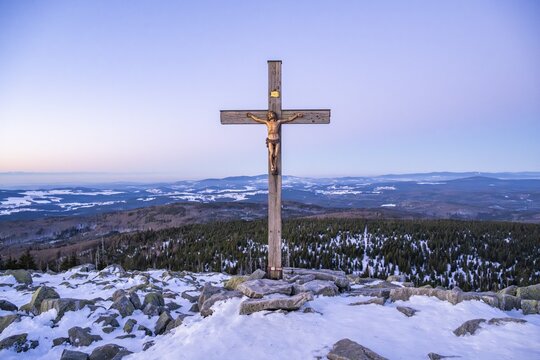 Christian cross on the peak of Mount Lusen with the view over the hills of the bavarian forest at sunrise at winter, Bavaria, Germany
