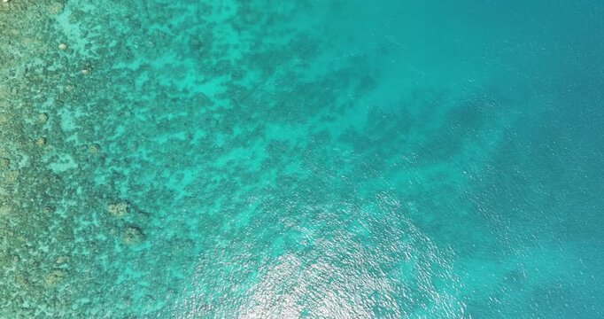 Aerial view of turquoise surface of the sea and the glare of the sun. Transparent ocean water surface.