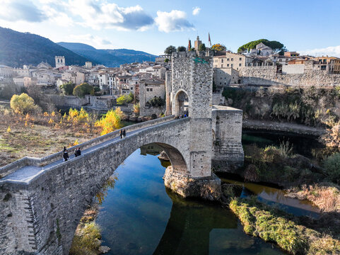 Aerial view of the historic medieval bridge, featuring stone arches and towers over the Fluvia river, surrounded by old town buildings in Besalu, Catalonia, Spain.