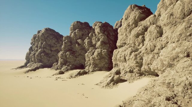 Beneath a clear azure sky, towering rock formations stand proudly against rolling dunes. Their rugged textures contrast beautifully with the smooth, golden sands surrounding them.