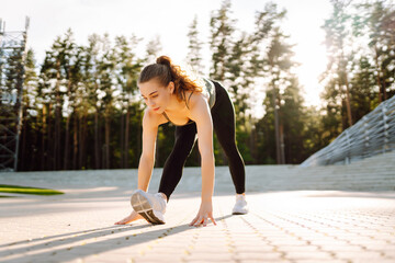 Obraz premium A young athlete trains on steps in the sun's rays. A woman in sportswear stretches or warms up at sunset. The concept of sport, enjoyment, and health.