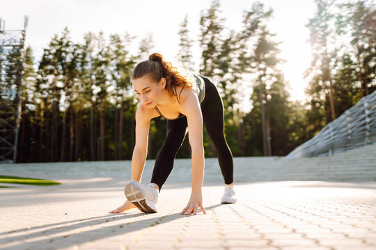 A young athlete trains on steps in the sun's rays. A woman in sportswear stretches or warms up at sunset. The concept of sport, enjoyment, and health.