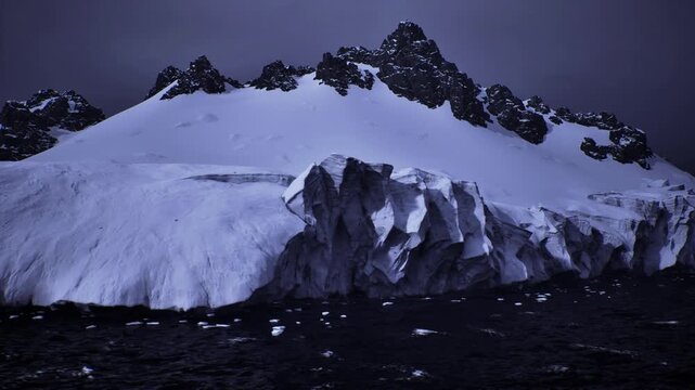 massive ice front with jagged seracs at night, brooding atmosphere with low cloud and heavy sea, waves beating against frozen cliffs, powerful visual