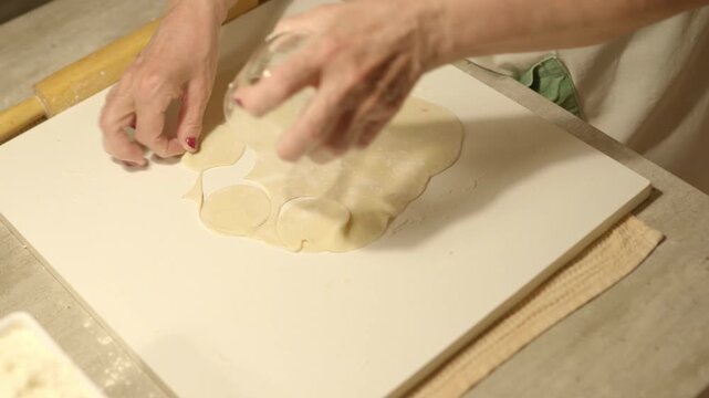 Woman&rsquo;s hands rolling dough for traditional pelmeni dumplings on flour-dusted kitchen table. Process of making homemade Russian food. Authentic culinary preparation and fresh dough kneading. 4K