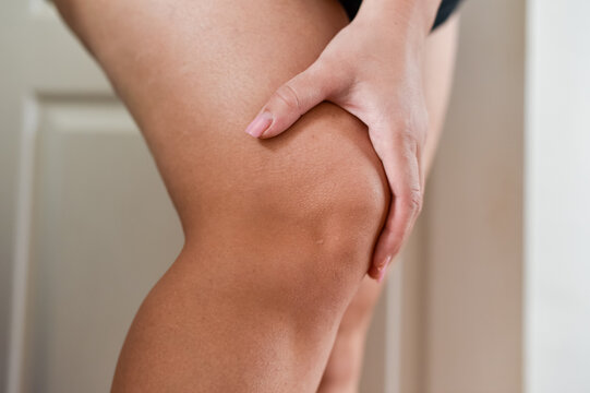 Close up of a female leg with a hand holding the thigh above the knee joint. The image shows the skin texture and anatomy of the human lower limb.