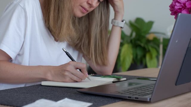 Woman writing expense notes while sitting at table with laptop euro cash and papers. Concept of household budget paying bills and money planning