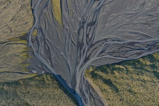 Aerial view of a complex braided river system with dark volcanic sediment channels winding through mossy green terrain in Vik, Myrdalshreppur, Iceland.