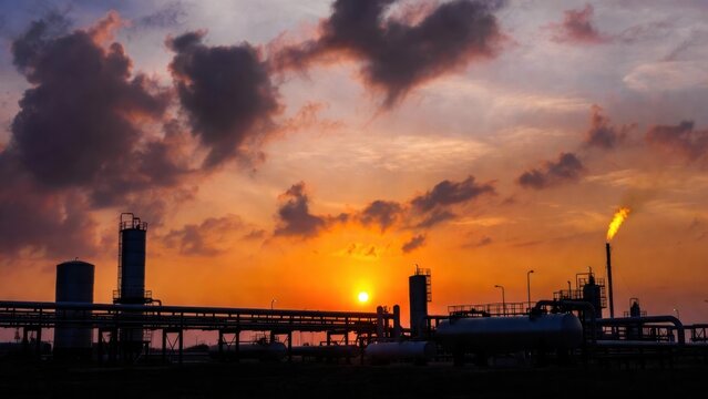 Industrial facility silhouetted at sunset with gas flare