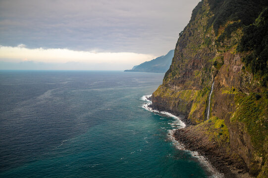 Dramatic coastline landscape with a waterfall cascading into the Atlantic Ocean in Madeira