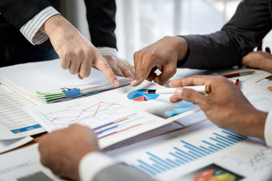 Three people are looking at a table with a lot of papers and graphs