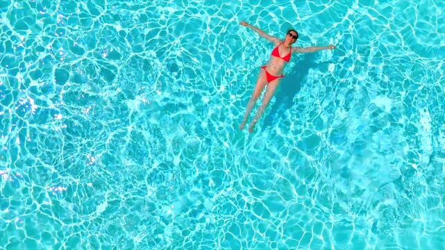 Top down view of a woman in pink swimsuit laying on her back in the pool.
